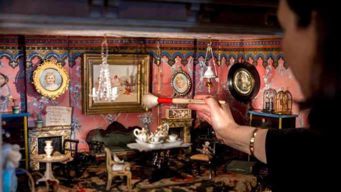Person using a brush to clean small antiques in a beautifully decorated room.
