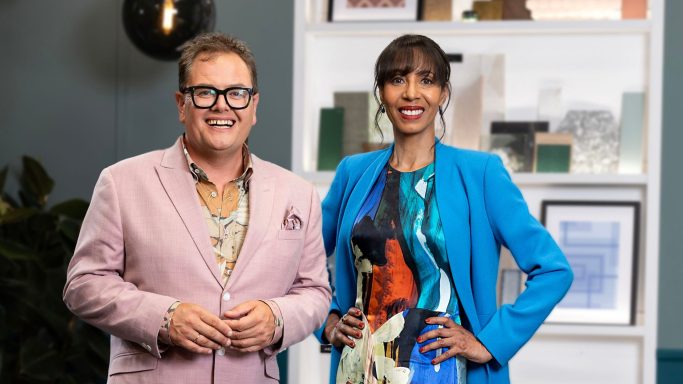Two presenters standing together, one in a pink suit and the other in a blue jacket, smiling.