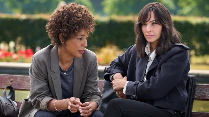 Two women sit on a bench in a park, engaged in a serious conversation.