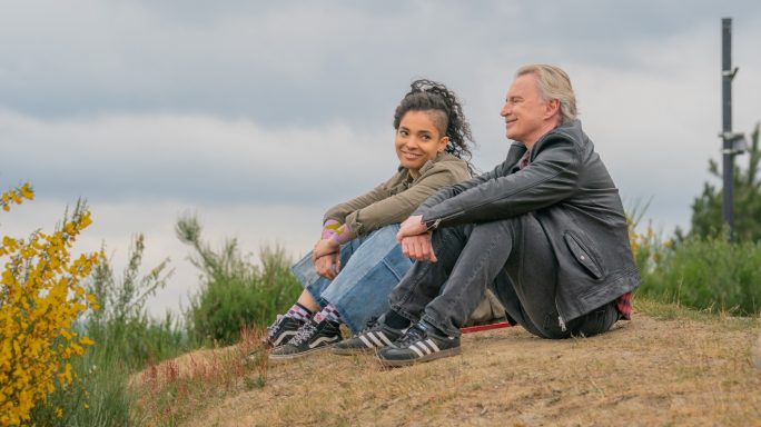 A man and woman sit on a hillside, smiling and enjoying each other's company.