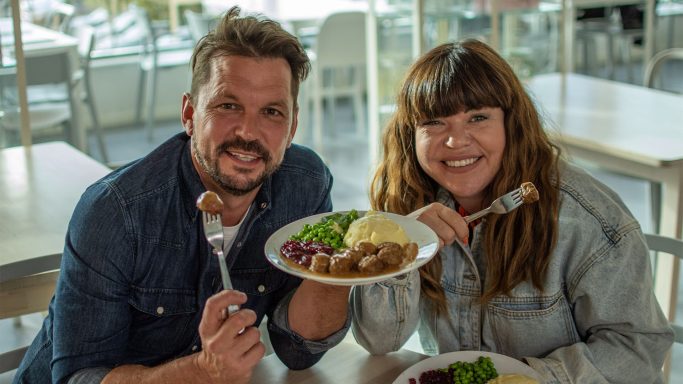 Man and woman smiling while holding plates of food in a casual dining setting.