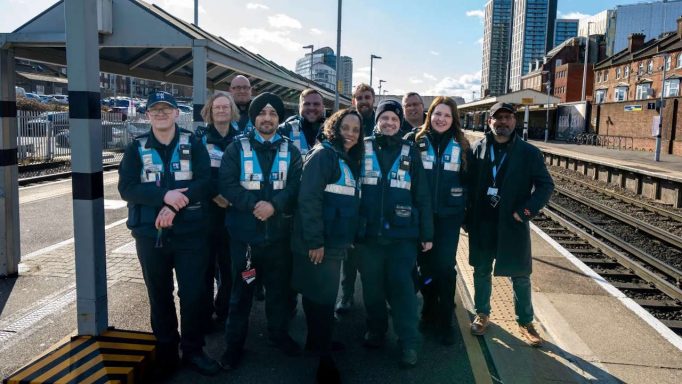 A group of rail staff posing together at a train station platform.