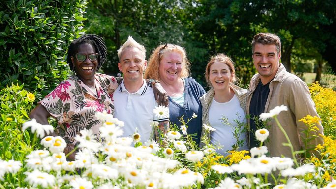 Five smiling individuals stand together in a vibrant flower garden.